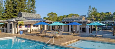 A pool area with lounge chairs and umbrellas, surrounded by trees and a building with solar panels.