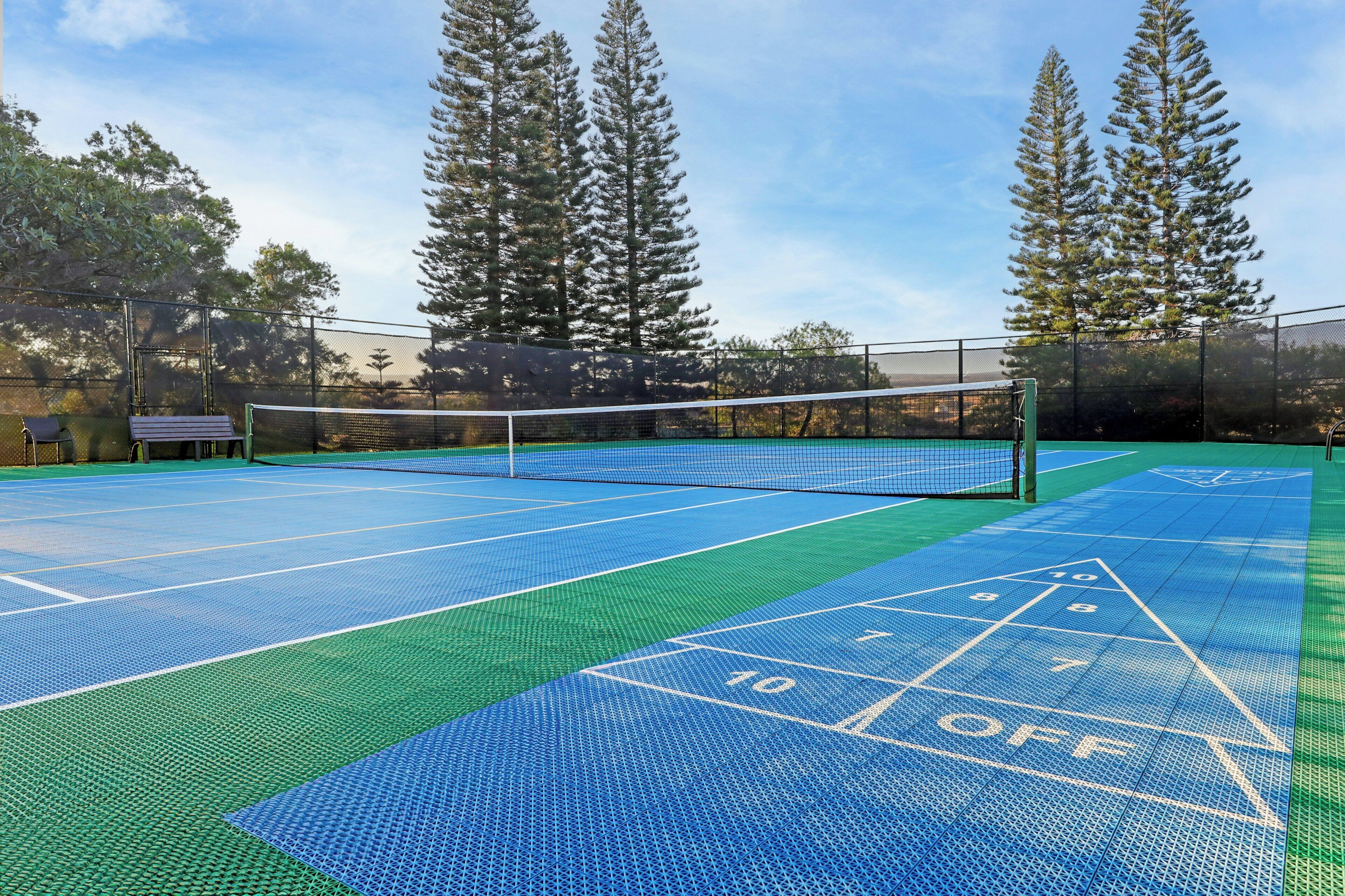 Una cancha de tenis al aire libre con una red, rodeada de árboles.