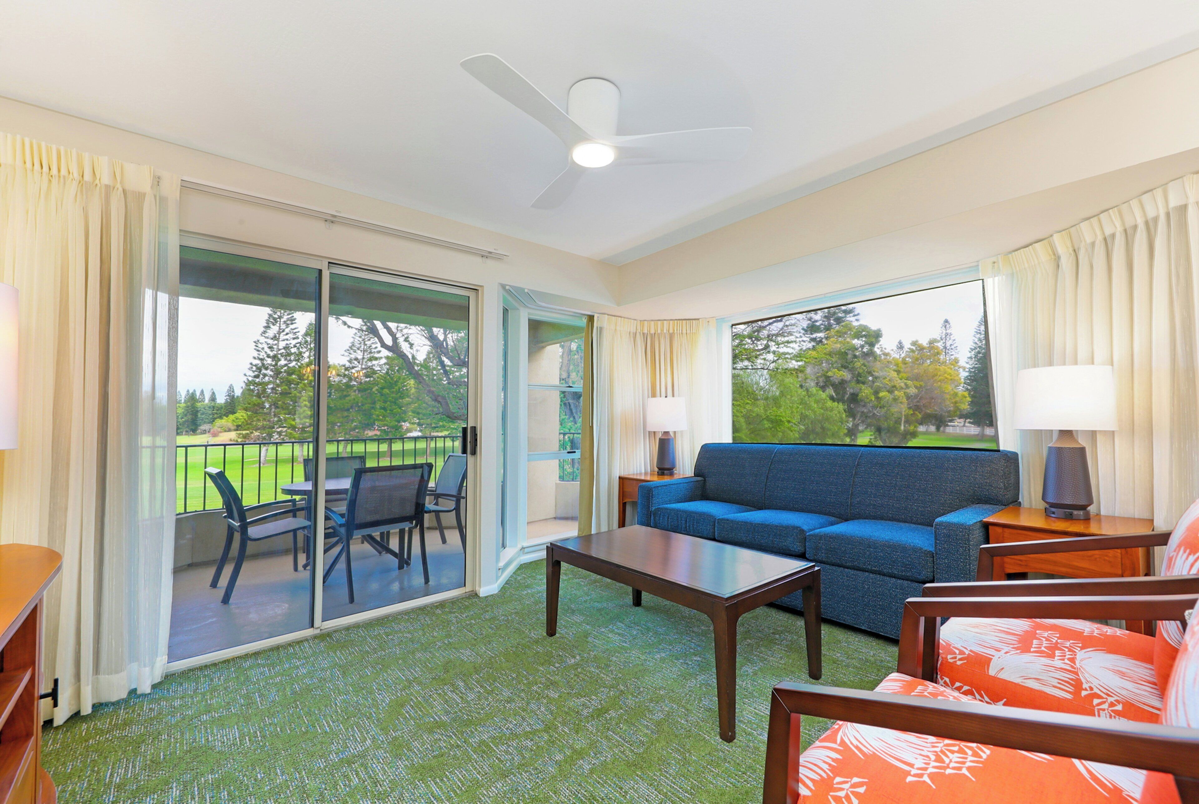 A hotel room with a balcony, a sofa, a table, and a chair.