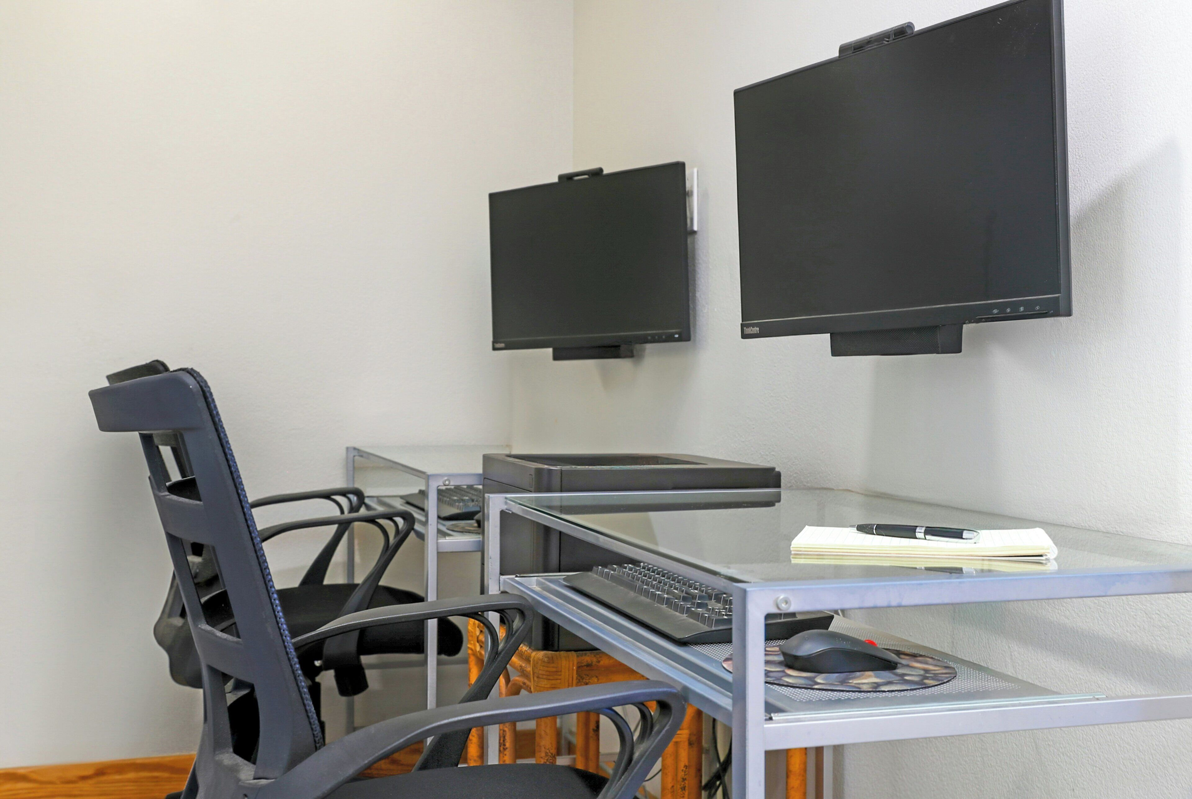A modern office space with a glass desk, two monitors, a keyboard, a mouse, and a chair.