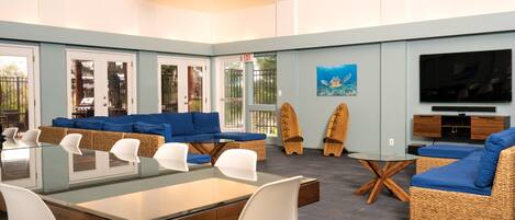 A spacious living area with a glass-top dining table, blue sofas, wicker furniture, and a television.