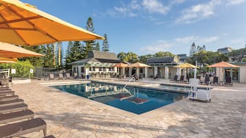 Relax by the clear blue pool surrounded by lounge chairs and tables, with a covered patio area nearby.