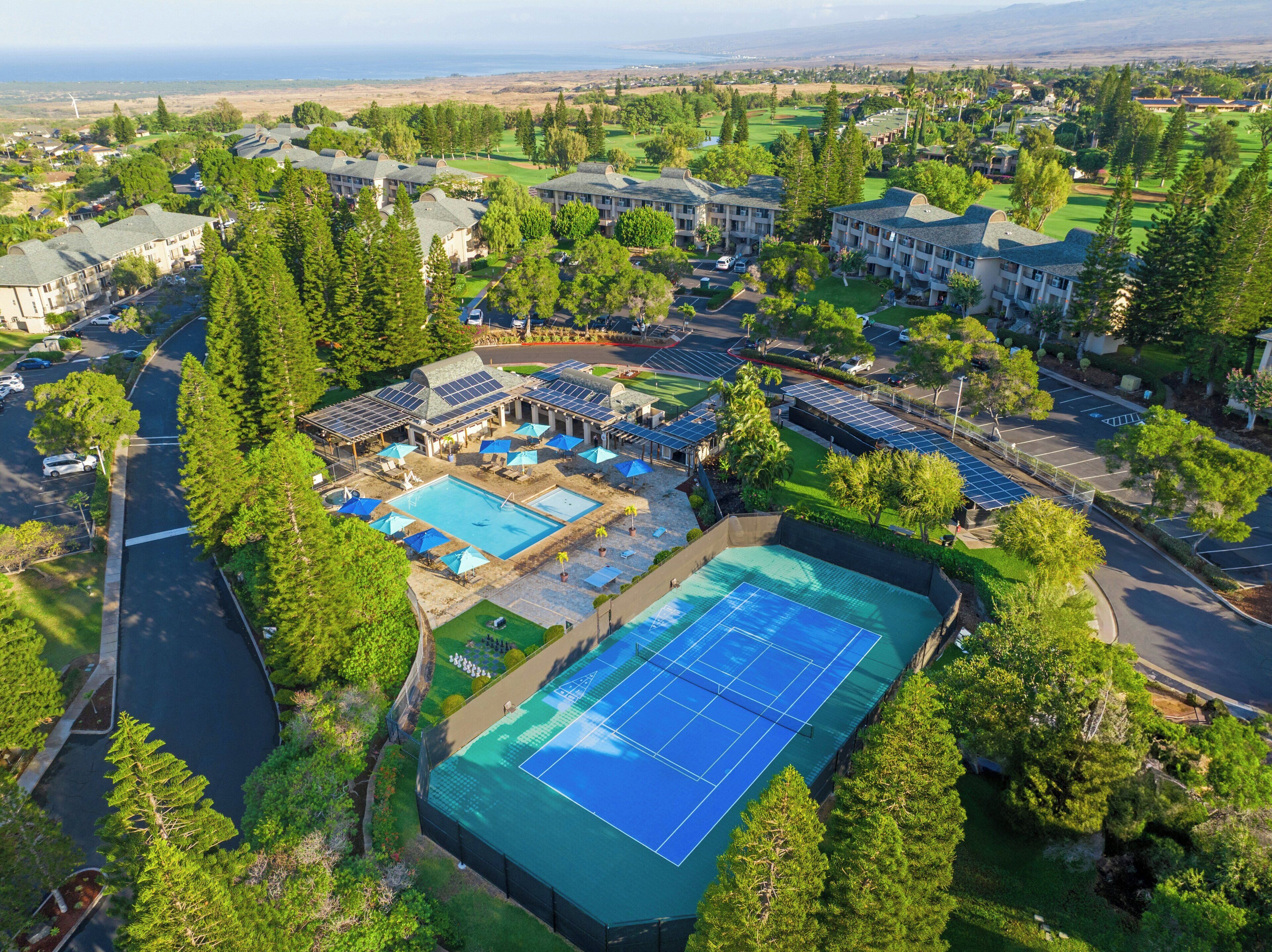 A resort with multiple buildings, a swimming pool, tennis courts, and solar panels.