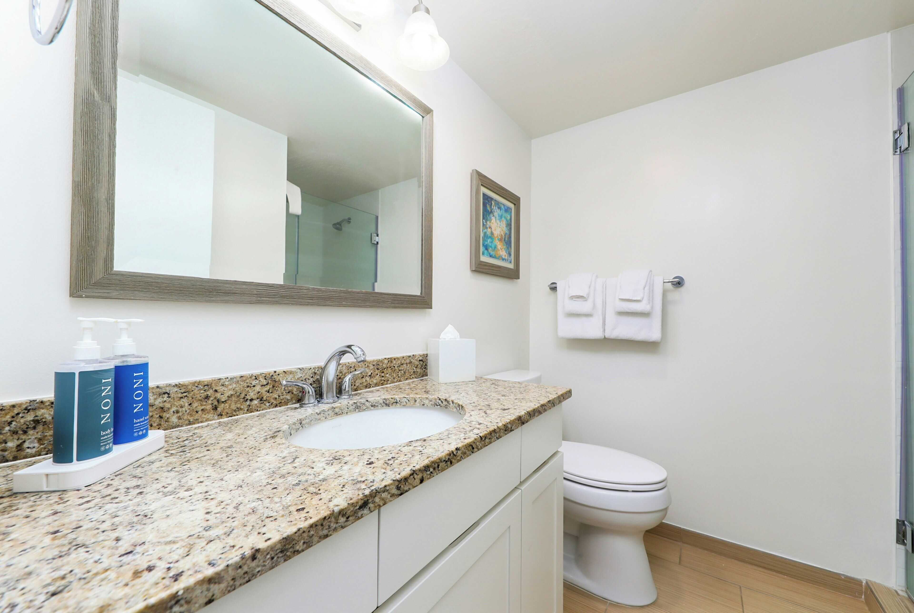 A bathroom with a granite countertop sink, a mirror, a toilet, and a shower.