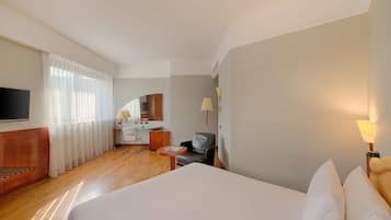 Ein Hotelzimmer mit einem großen Bett, einem Schreibtisch, einem Sessel, einem Fernseher und einer Lampe.