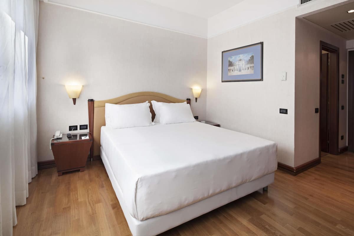 A hotel room with a large bed, bedside tables, a phone, and a framed picture on the wall.