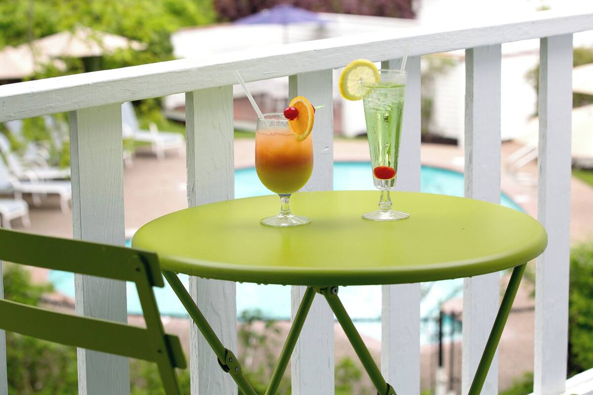A green table with two drinks on a balcony overlooking a swimming pool.