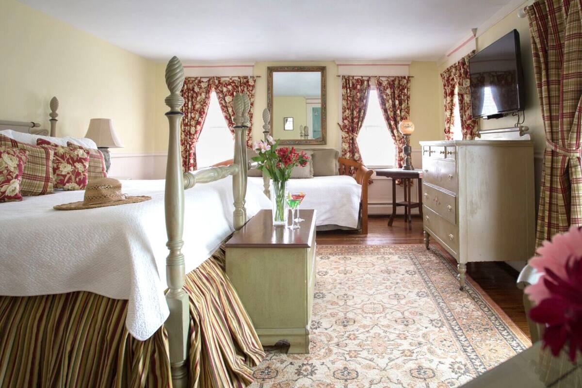 A hotel room with a bed, a desk, a dresser, a television, and a window with curtains.