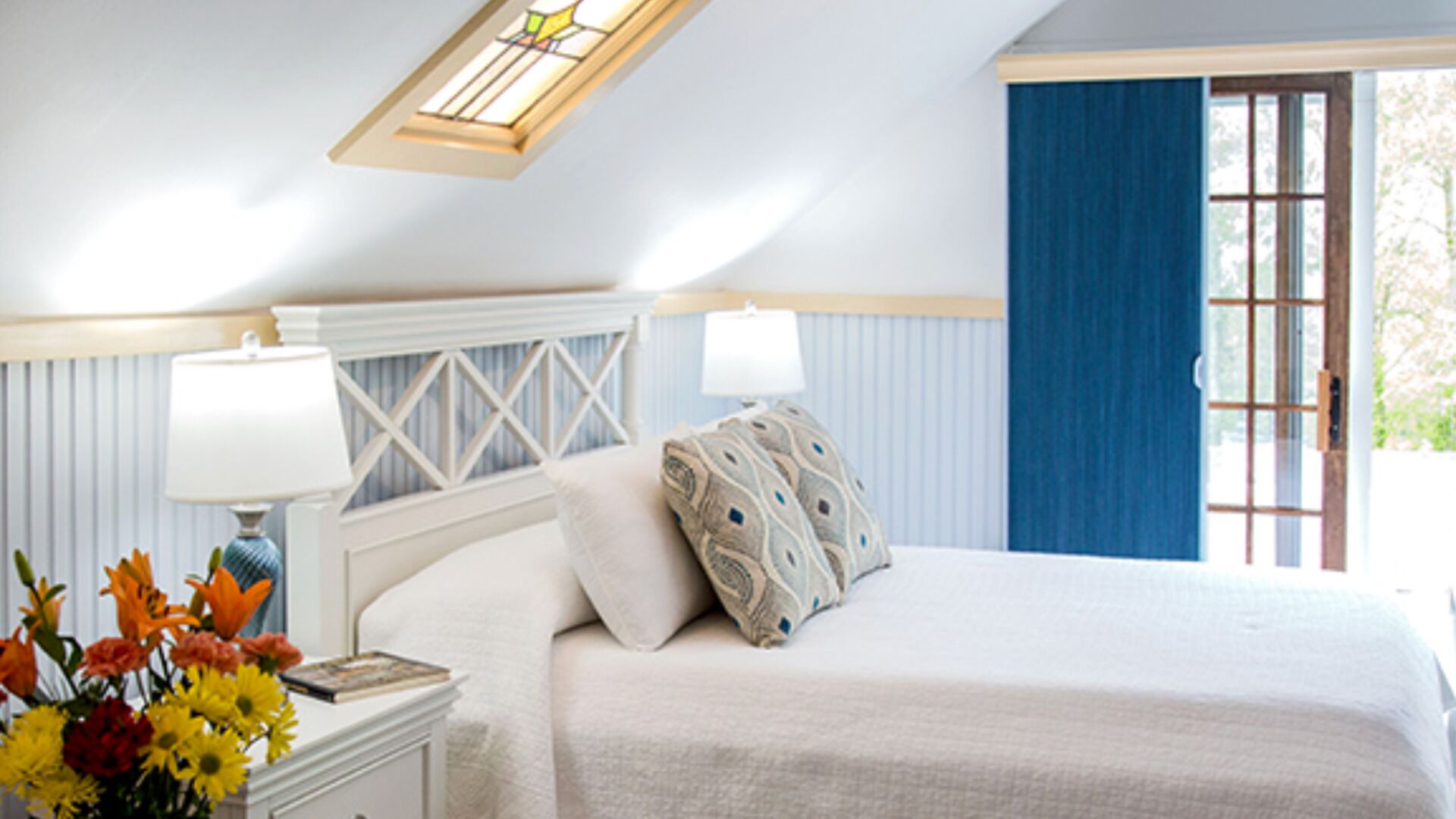 Une chambre à coucher avec un lit, deux lampes de chevet, une table de chevet, un vase de fleurs et une fenêtre avec des rideaux.