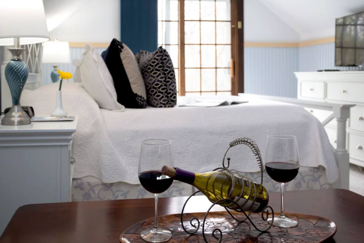 A hotel room with a bed, a TV, a dresser, and a table with two wine glasses and a bottle.