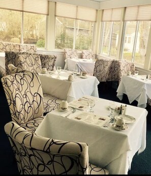 A dining area with tables set for service, patterned upholstery, and large windows.