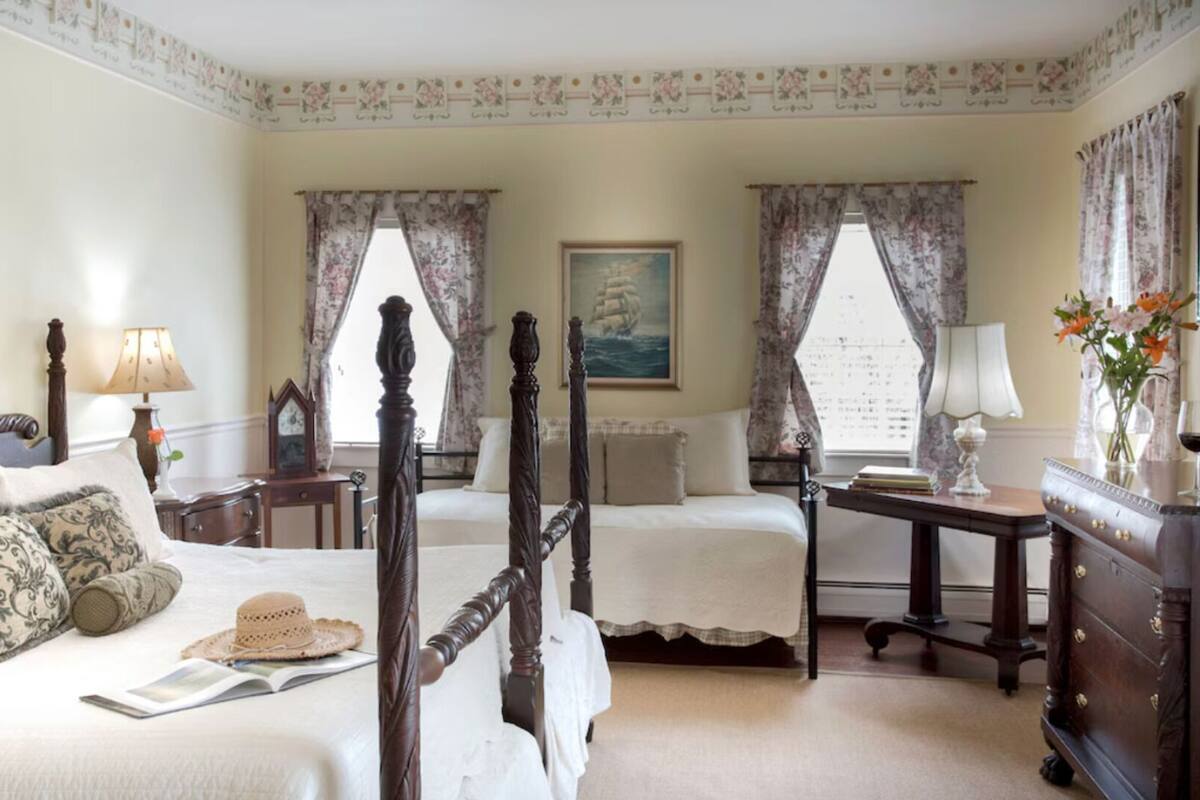 A traditional bedroom with two beds, a dresser, a nightstand, and a painting on the wall.