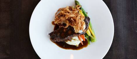 A white plate with a piece of meat, mashed potatoes, and vegetables on a dark surface.