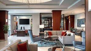 A spacious living area with a large sofa, armchairs, and a coffee table. There is a TV mounted on the wall and a dining area in the background.