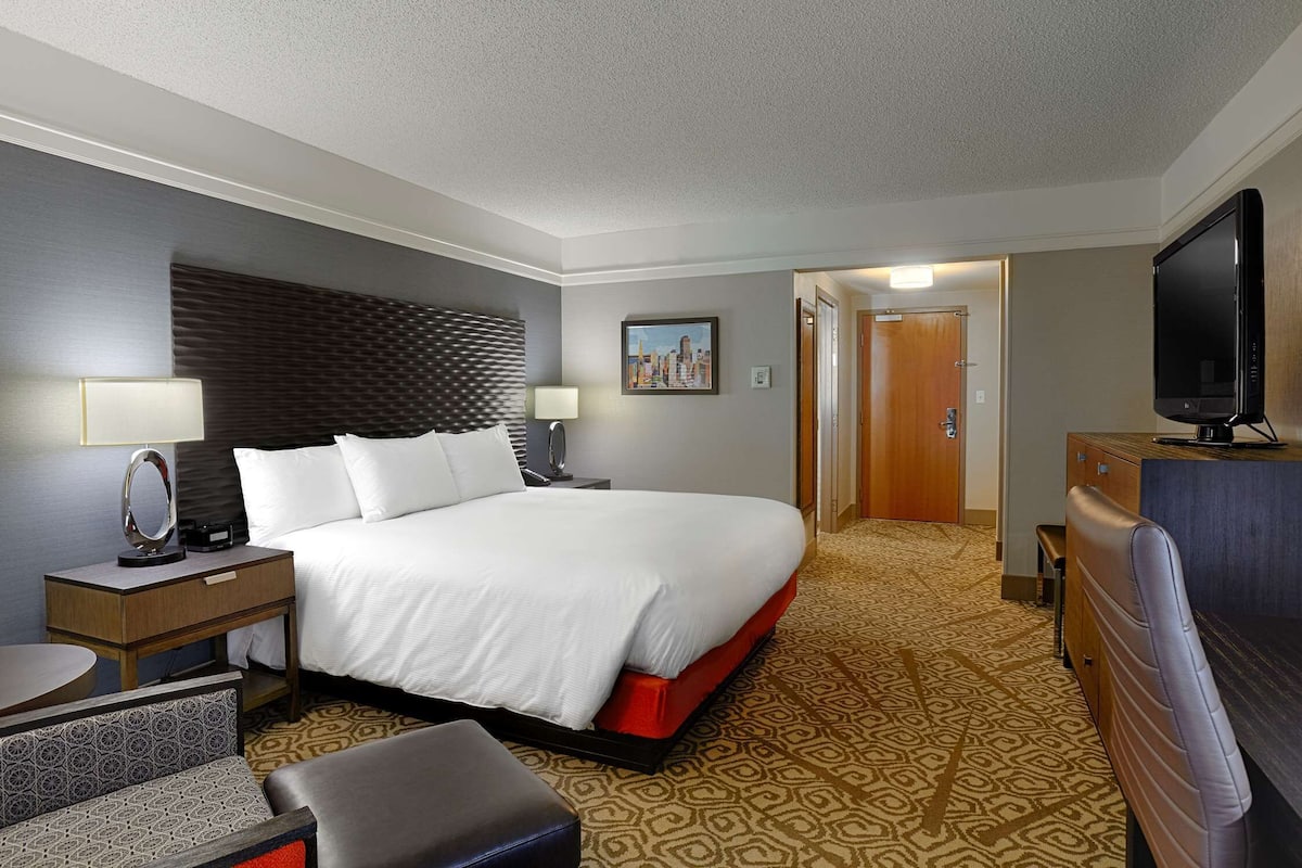 A hotel room with a large bed, bedside tables with lamps, a television, and a patterned carpet.