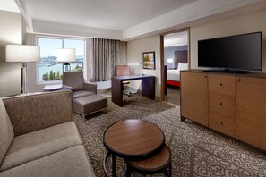 Een hotelkamer met een groot raam, een flatscreen televisie, een bureau, een bank en een kamerbreed tapijt met een patroon.