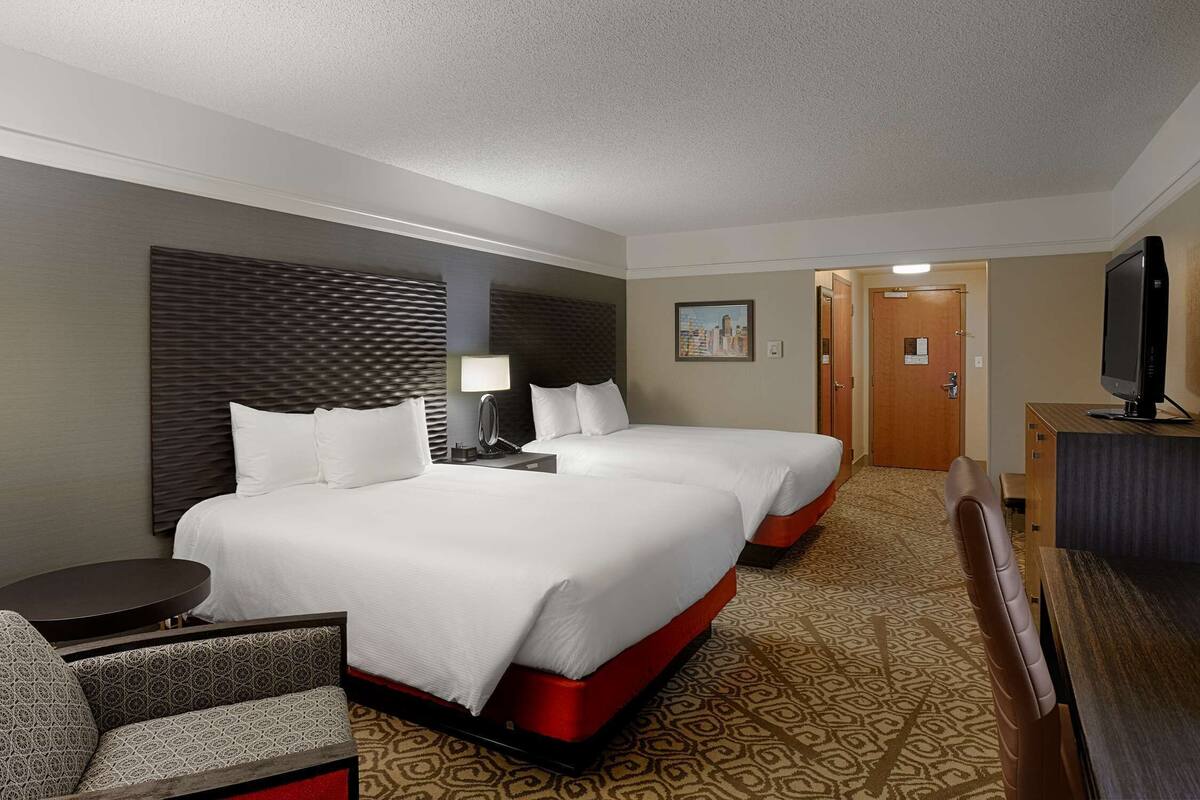 A hotel room with two beds, a desk, a chair, a TV, and a patterned carpet.