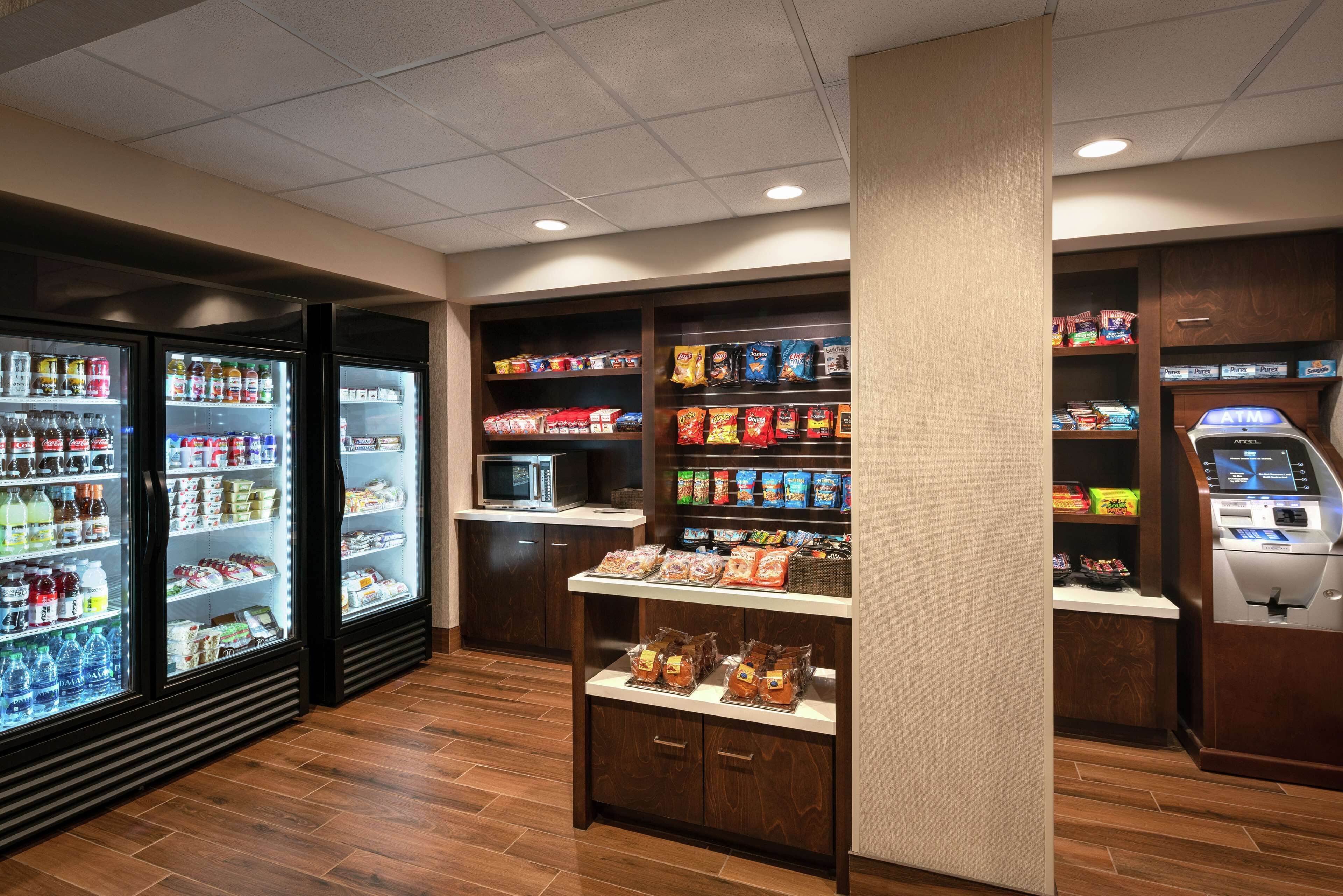 A self-service kiosk area with refrigerated beverage dispensers, snack shelves, and an ATM.