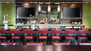 A bar area with multiple seating options, a variety of liquor bottles, and two large flat-screen TVs mounted on the wall.