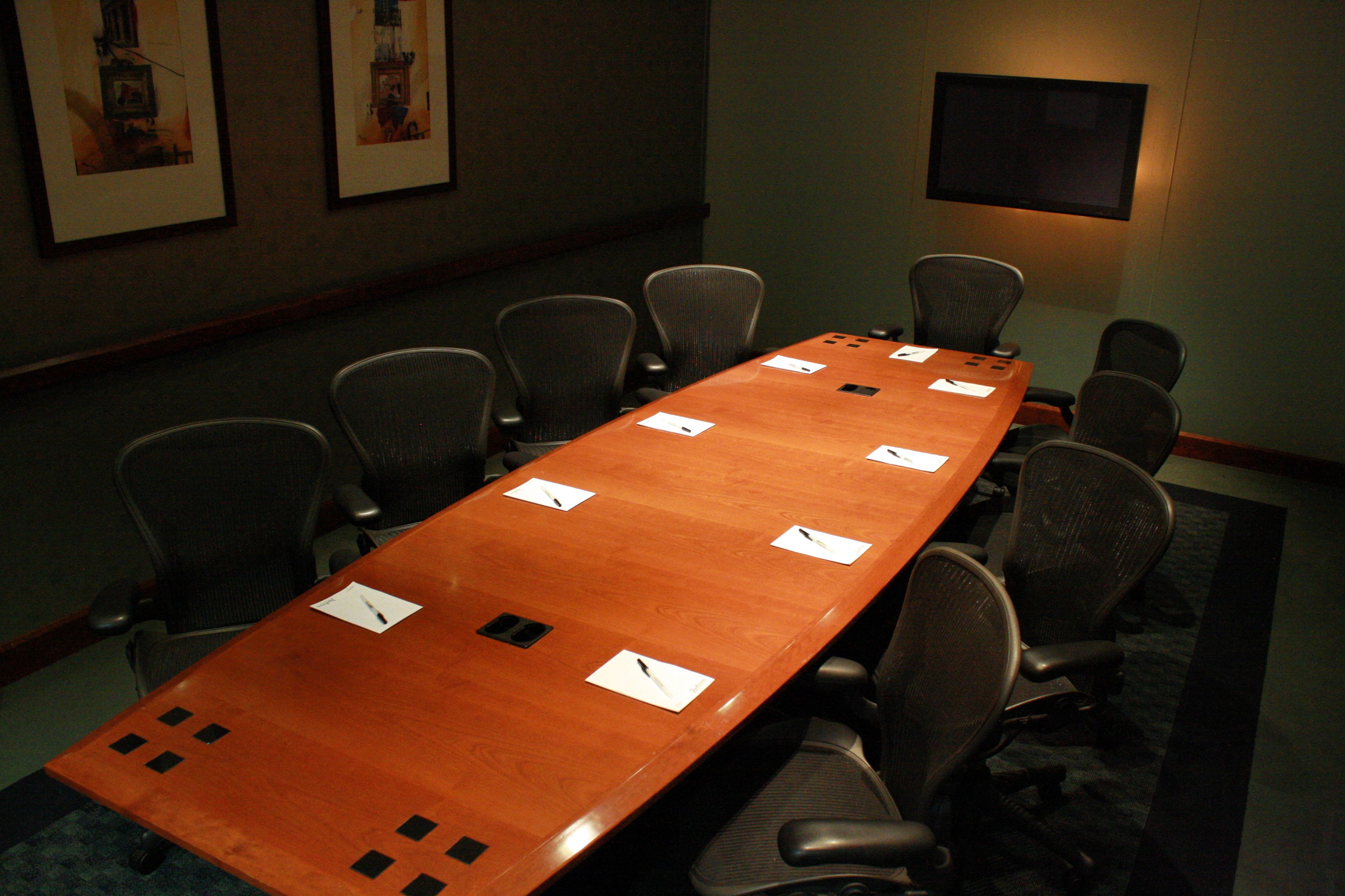 A conference room with a long table, eight chairs, and framed pictures on the wall.