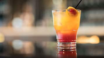 A glass of layered cocktail with a cherry garnish on a reflective surface.