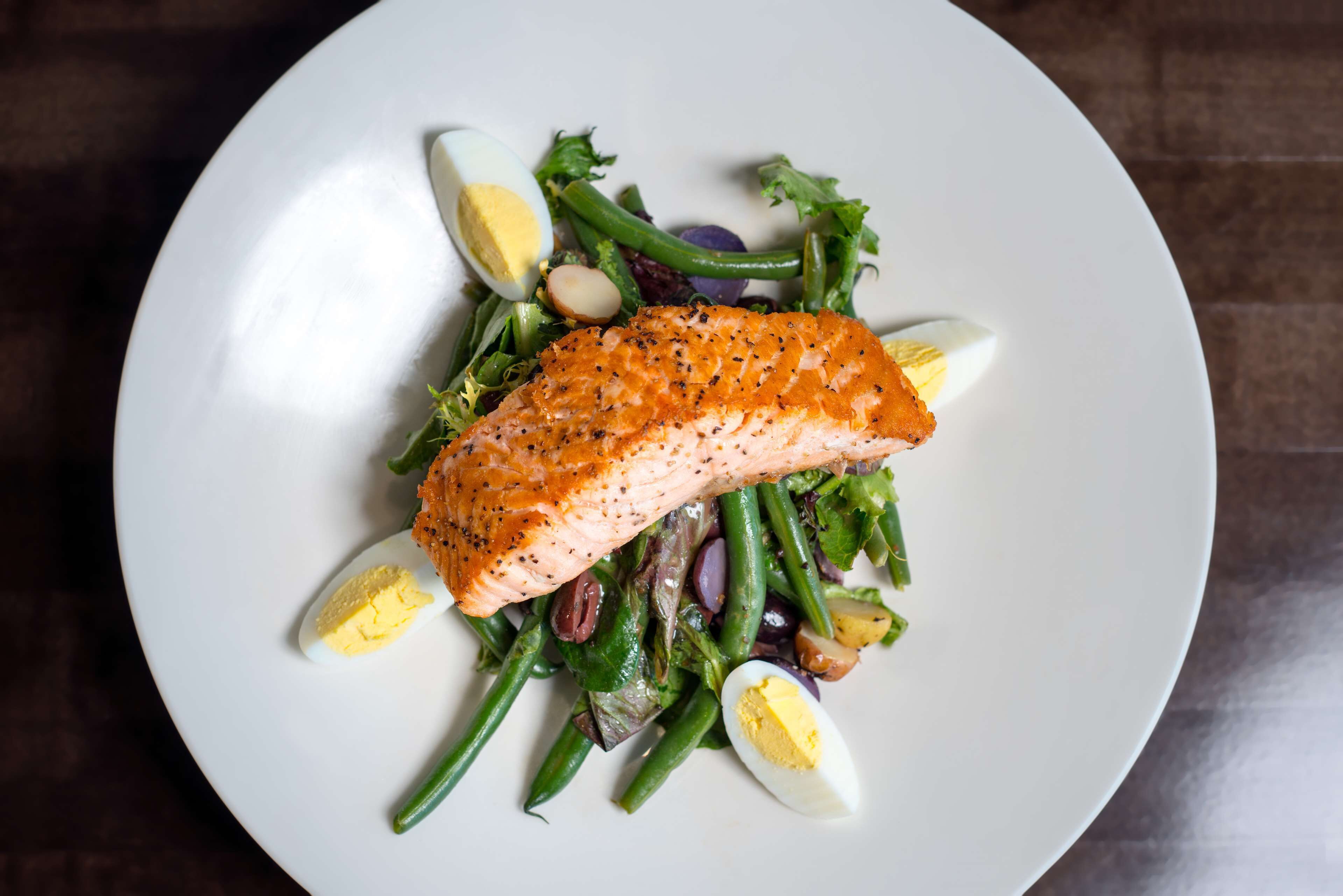 A plate with salmon, green beans, and boiled eggs.