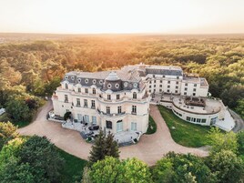 Un edificio grande e histórico con varias alas y un patio central, rodeado de un bosque denso.