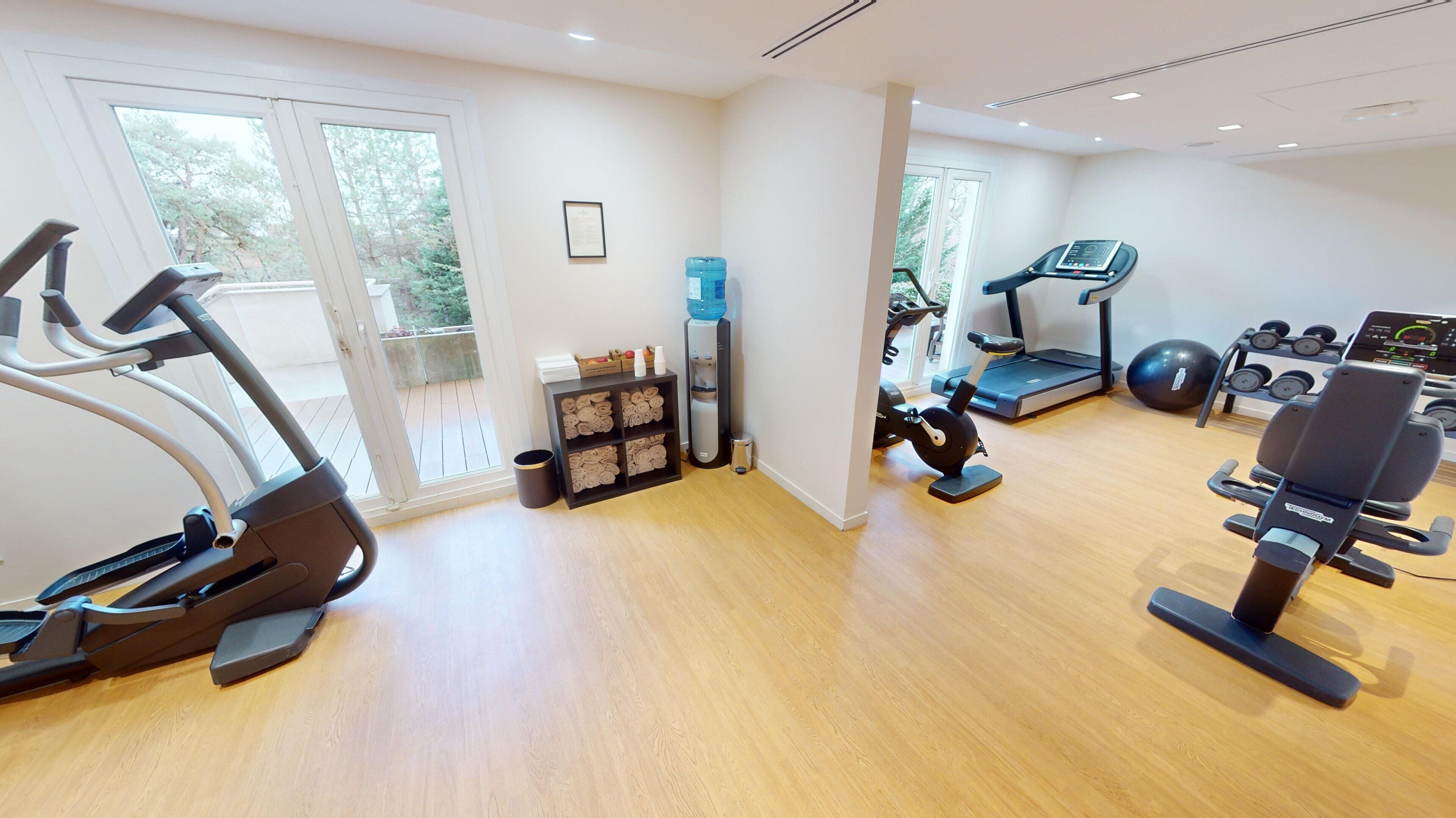 Une salle de sport équipée d’appareils de cardio, d’un distributeur d’eau et d’un tapis de course.