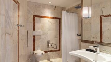 Un baño moderno con piso de mármol, un lavamanos blanco con espejo, una ducha con cabezal de ducha de mano y un inodoro con barra de apoyo.