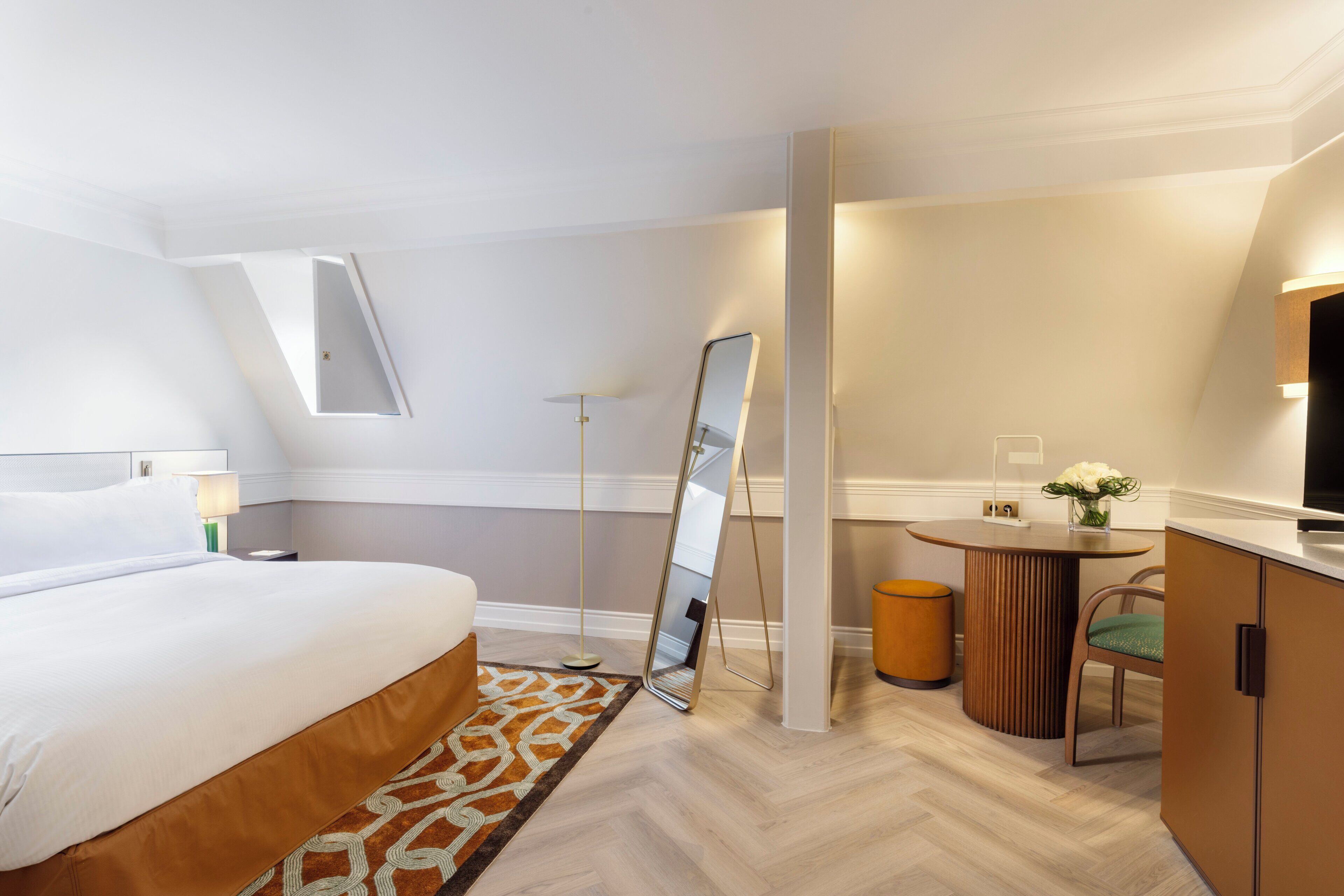 Et moderne hotelværelse med en seng, et rundt bord, en stol, et spejl og et fjernsyn.
