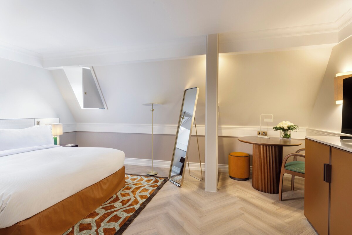 Una habitación de hotel moderna con una cama, una pequeña mesa redonda, una silla, un espejo y un televisor.
