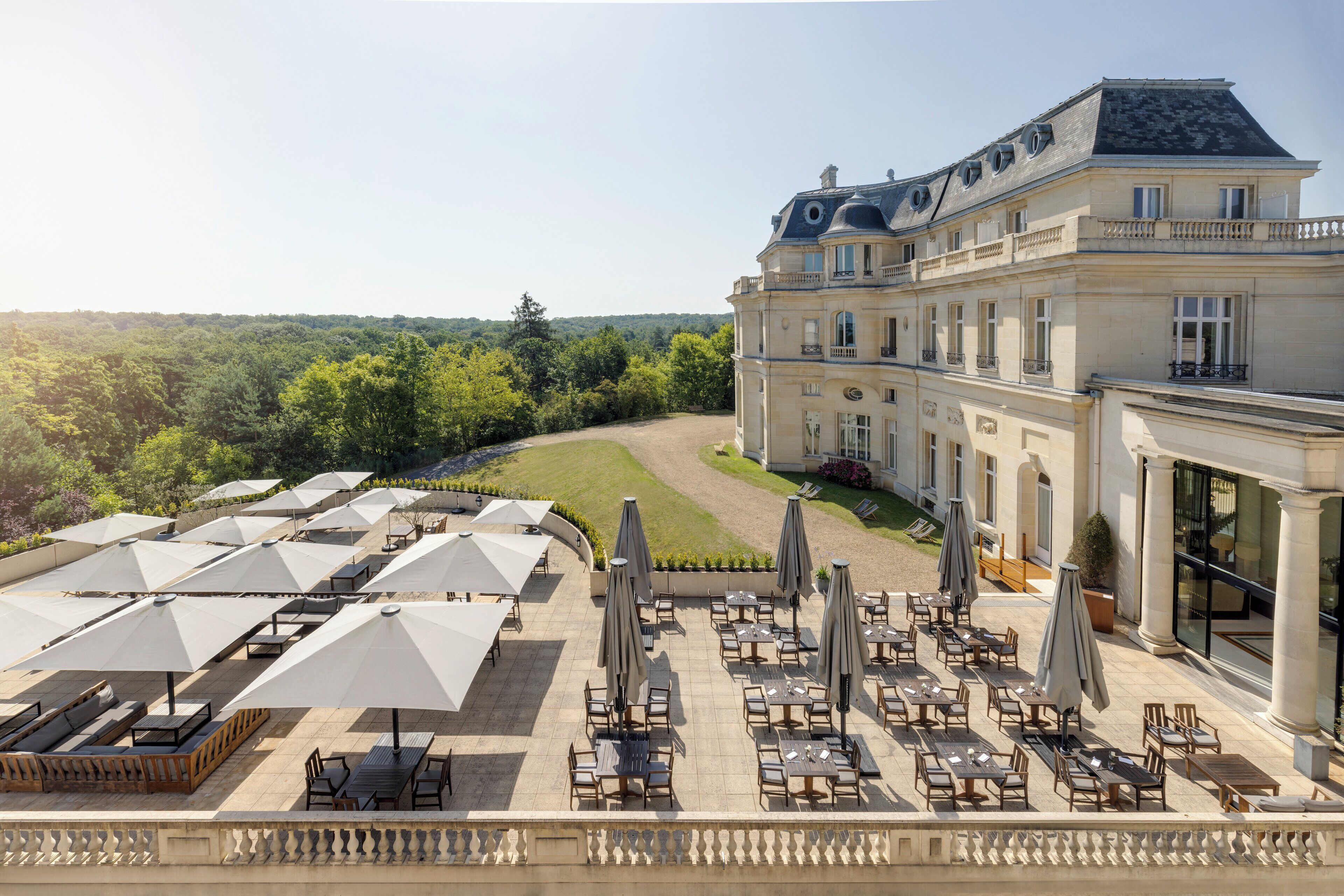 A large building with a formal exterior, a courtyard with outdoor seating, and a view of the surrounding forest.