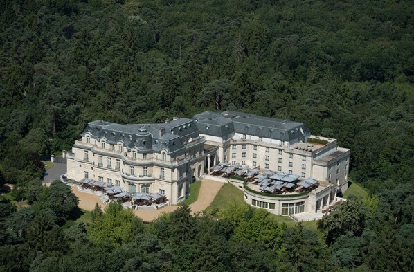 A large, historic hotel with multiple wings and a central courtyard, surrounded by dense forest. - InterContinental Chantilly Chateau Mont Royal by IHG (La Chapelle-en-Serval)