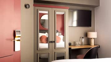 A hotel room with a bed, a desk with a lamp, a TV, and a wardrobe with mirrors.