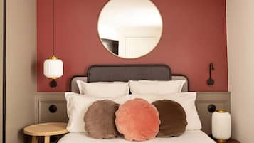 Une chambre avec un miroir rond, un lit avec de nombreux coussins, une table de chevet et une lampe fixée au mur.