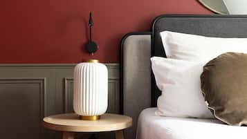 Una cama bien hecha con almohadas blancas y marrones, una mesita de noche redonda de madera con una lámpara blanca y un reloj de pared.