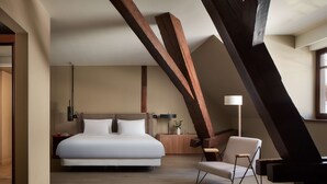A modern hotel room with a large bed, a wooden chair, and exposed beams.