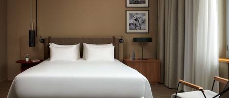 Una habitación de hotel moderna con una cama grande, dos mesitas de noche, una silla y dos cuadros en la pared.