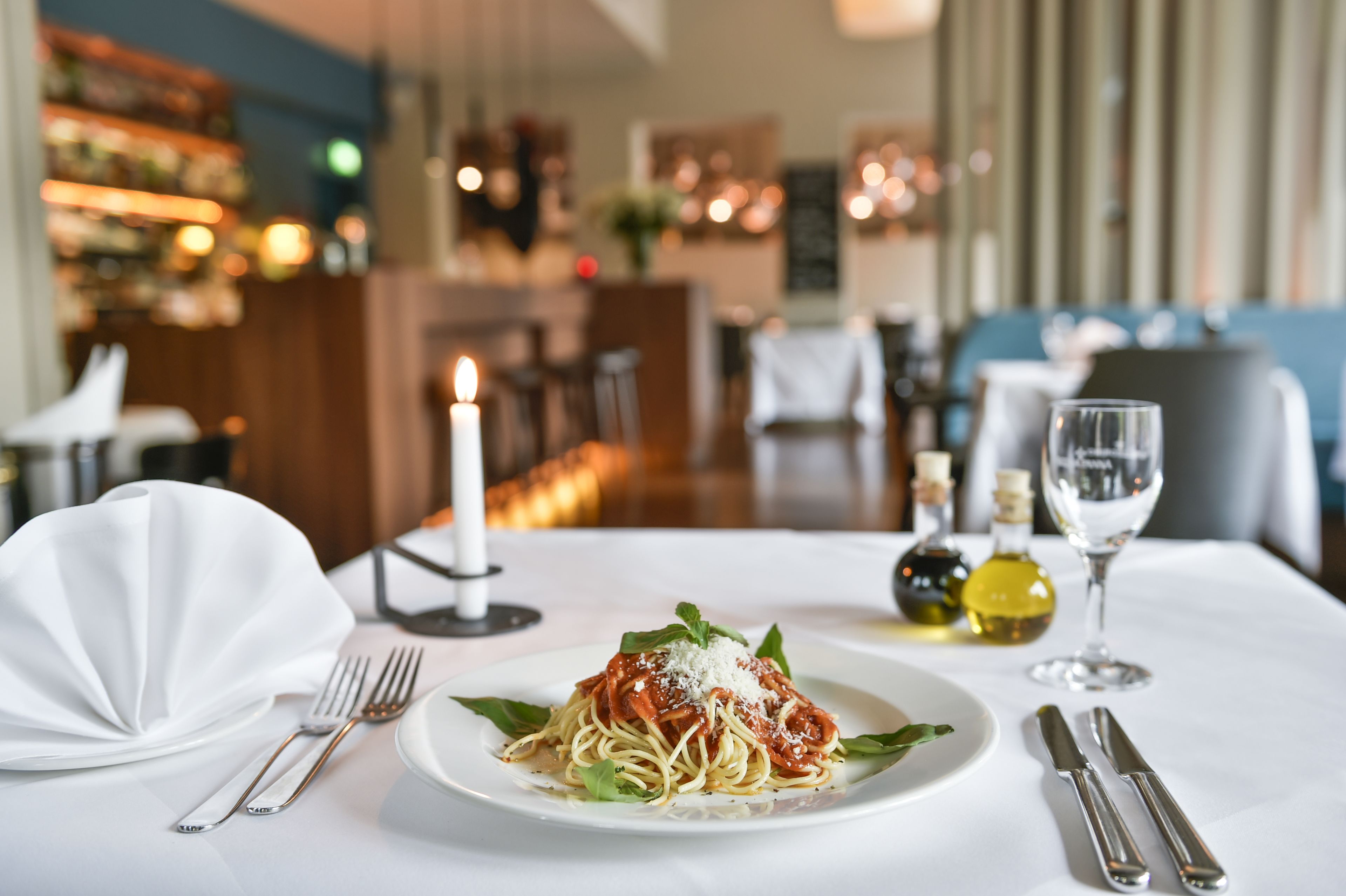 A dining table with a plate of spaghetti, a wine glass, and cutlery.