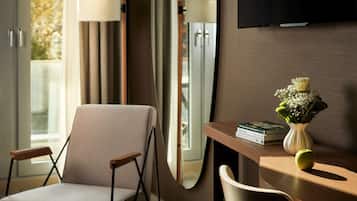A modern hotel room with a comfortable chair, a wooden desk, a vase with flowers, and a flat-screen TV on the wall.