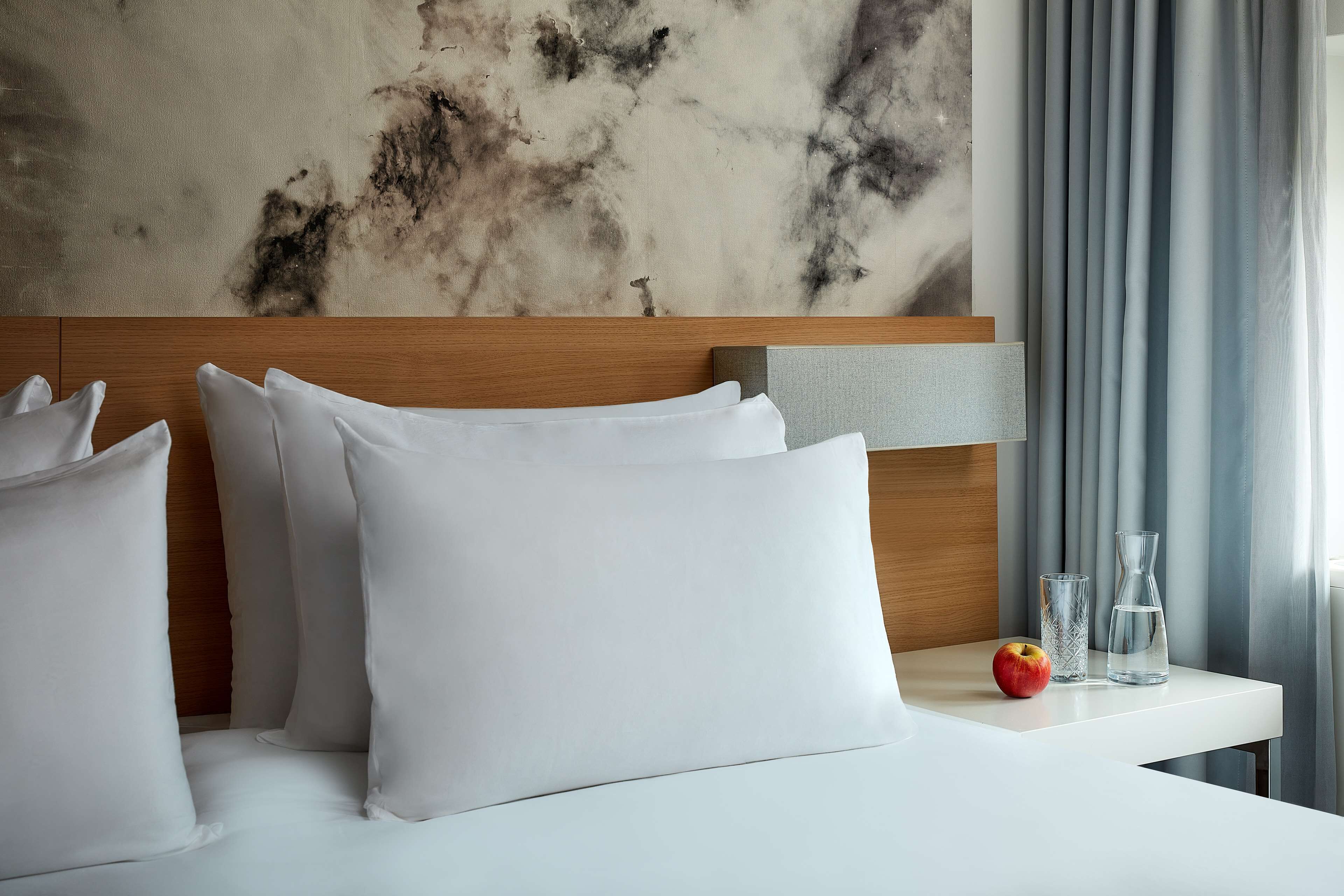 Une chambre d’hôtel avec une tête de lit en bois, du linge de lit blanc et un mur en marbre.