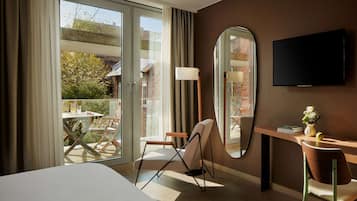 A hotel room with a large bed, a desk with a chair, a TV mounted on the wall, and a sliding glass door leading to an outdoor area.