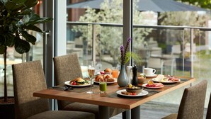 A breakfast table set with plates of food, a glass of juice, and a vase with flowers. - NH Collection Heidelberg (Heidelberg)