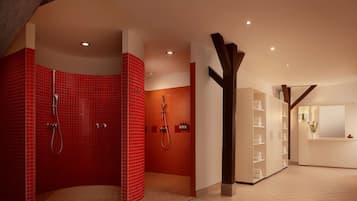 Un baño moderno con zona de ducha con azulejos rojos, suelo de madera y un mostrador de recepción con un jarrón de flores.