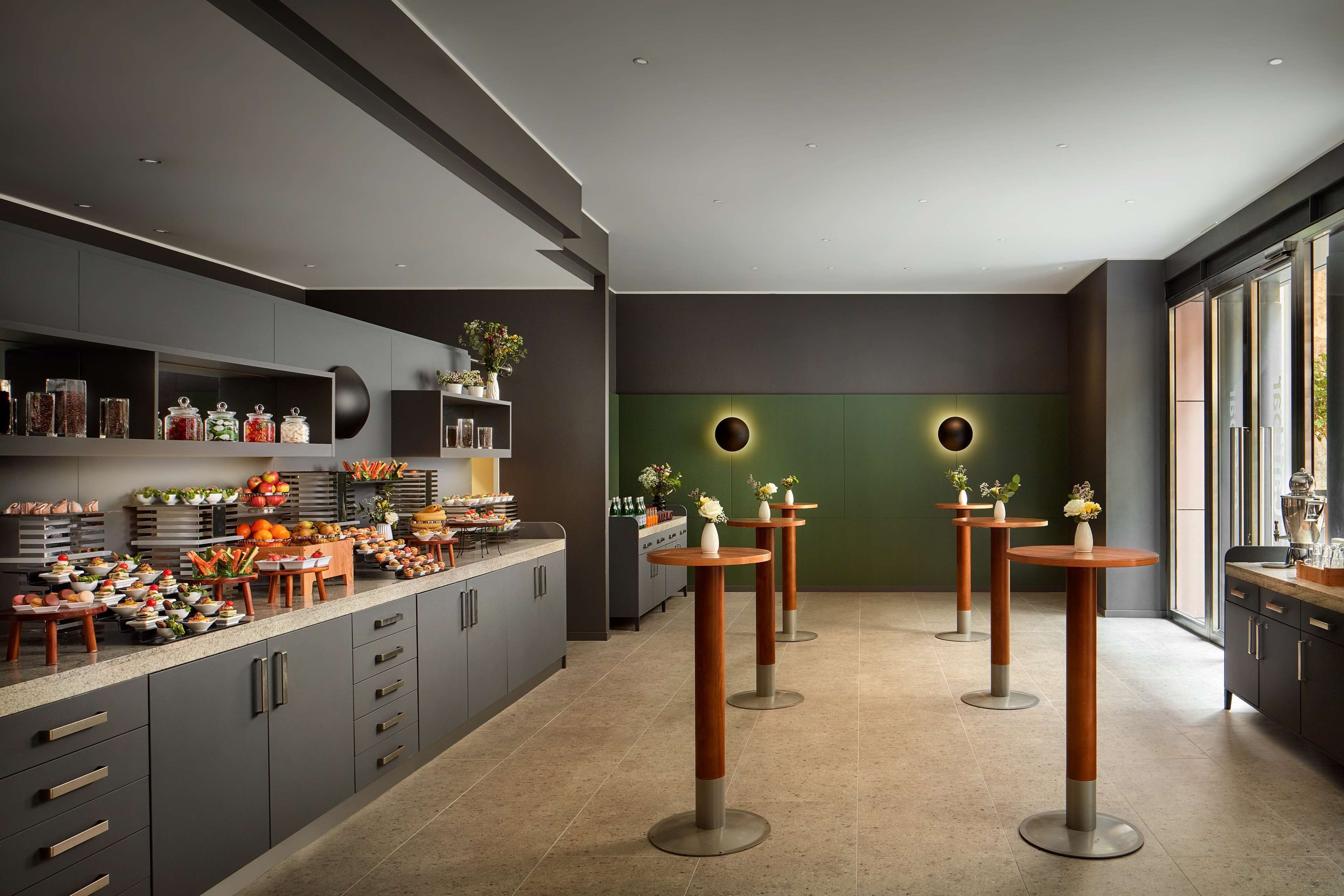 Een moderne keuken met grijze kastjes, een centraal eiland met etenswaren, en drie ronde tafels met vazen.
