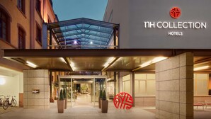 The entrance of NH Collection Hotels with a glass facade, a signboard, and a large red logo. - NH Collection Heidelberg (Heidelberg)