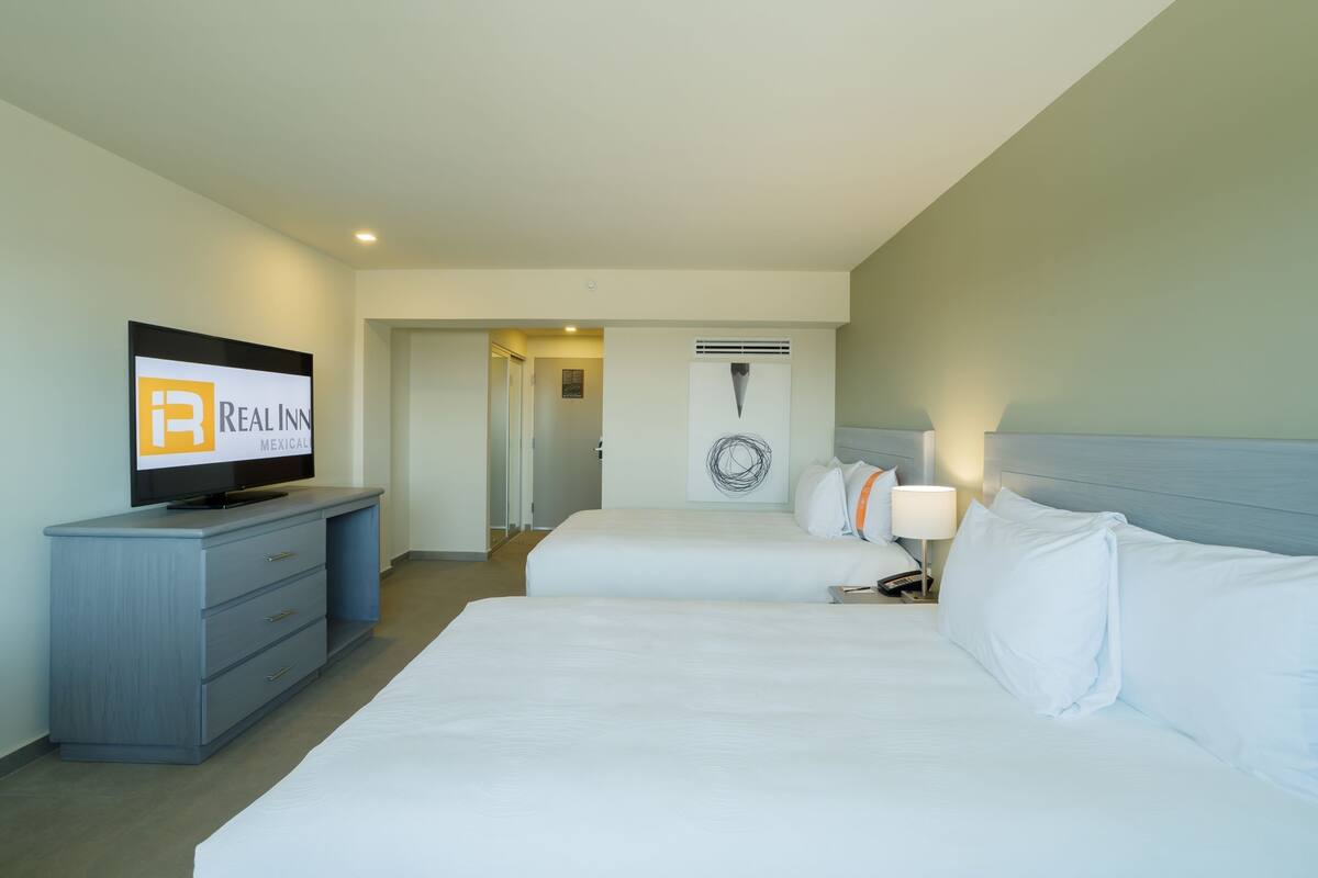 Habitación de hotel con dos camas, televisión, escritorio y una obra de arte colgada en la pared.