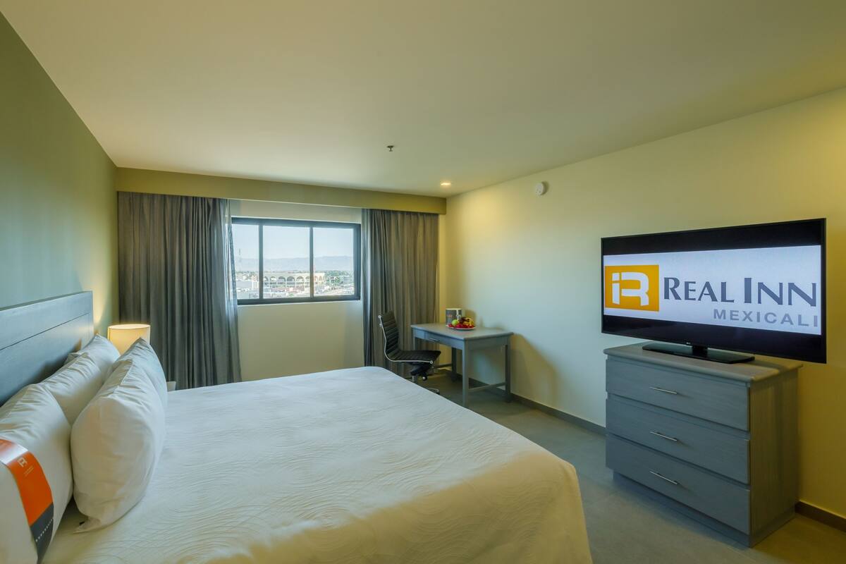 Habitación de hotel con cama, escritorio, televisor y vistas a la ciudad.