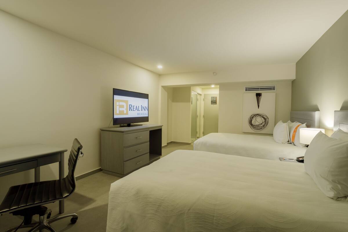 Habitación de hotel con dos camas, un escritorio, un televisor y un aire acondicionado de pared.