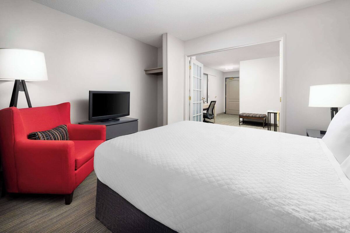 Une chambre d’hôtel avec un grand lit, un fauteuil rouge, une télévision et un bureau.